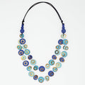 A double-strand necklace featuring blue and turquoise evil eye beads with gold accents, suspended on a black cord, shot against a plain white background.