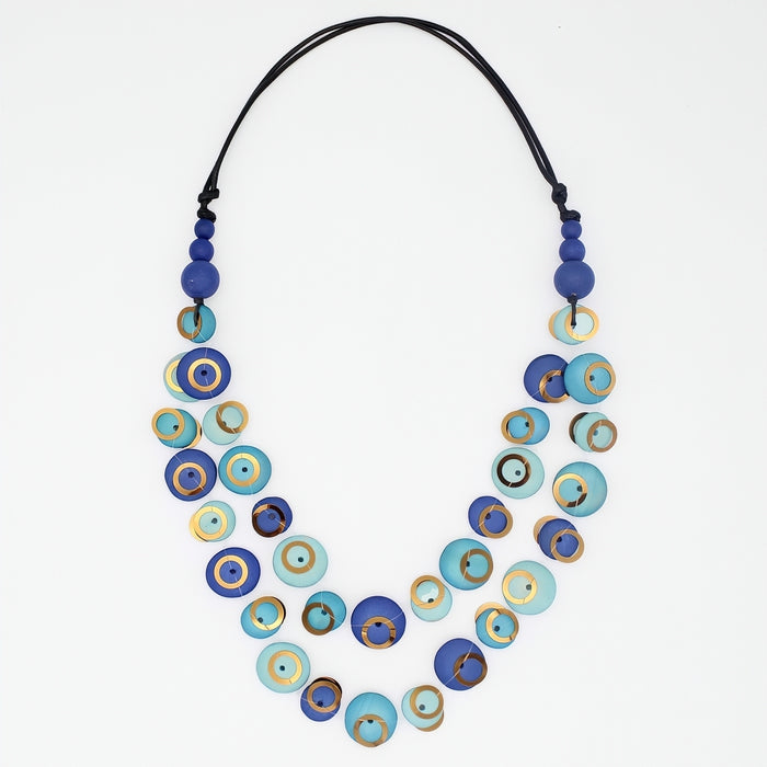 A double-strand necklace featuring blue and turquoise evil eye beads with gold accents, suspended on a black cord, shot against a plain white background.