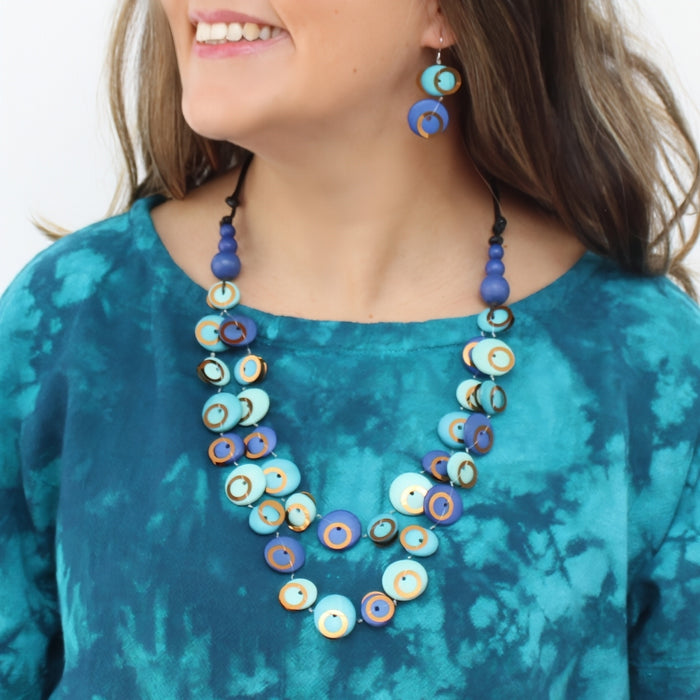 Woman wearing a blue and gold beaded necklace and earrings on a white background