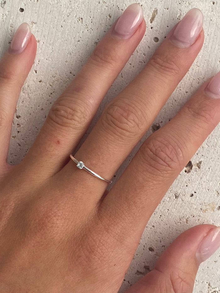 A silver dainty ring with a topaz light blue stone.