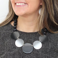 Necklace with black and silver circular pendants worn by a person