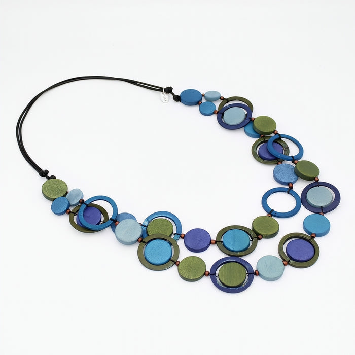 A multi-strand statement necklace featuring circular wooden beads in shades of blue, green, and purple, strung on a black cord, displayed on a clean white background.