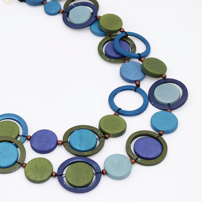 A multi-strand geometric necklace featuring circular wooden beads in shades of blue, green, purple, and light blue, separated by small copper-colored spacer beads, on a plain white background.