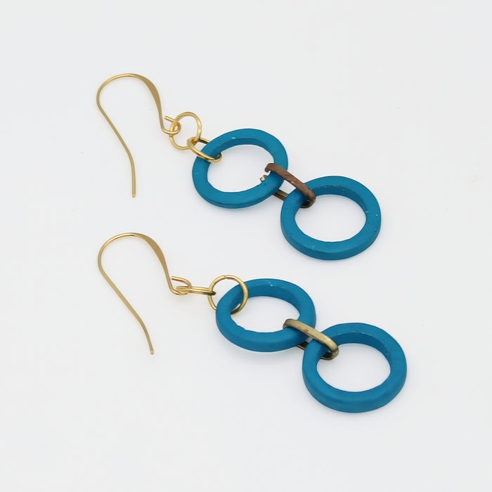 Close-up of an ear wearing turquoise double-circle earrings on a neutral background