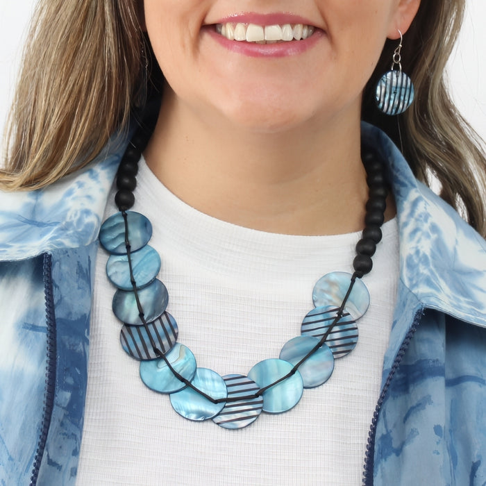 Woman wearing a blue and black beaded necklace with a white shirt and blue jacket.