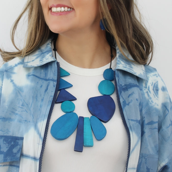 Woman wearing a blue and white patterned jacket with a large blue necklace.