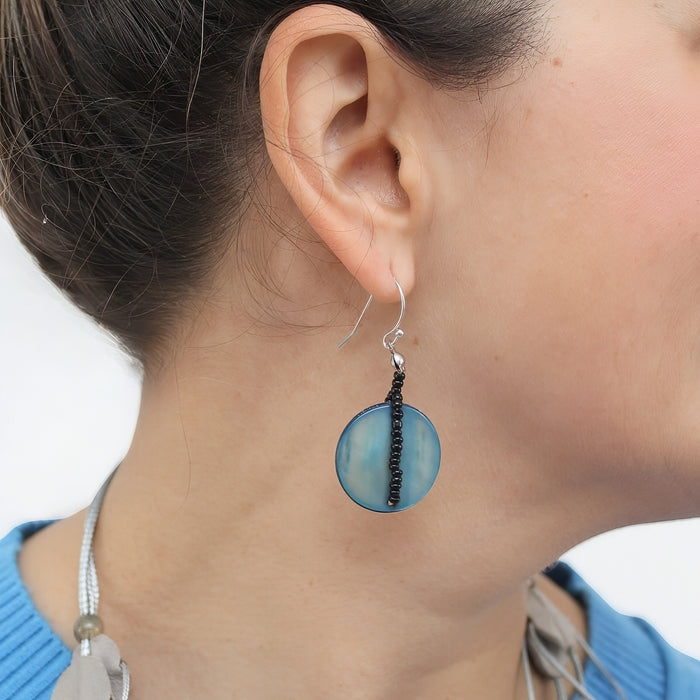 Close-up of a person wearing blue circular earrings with black thread.