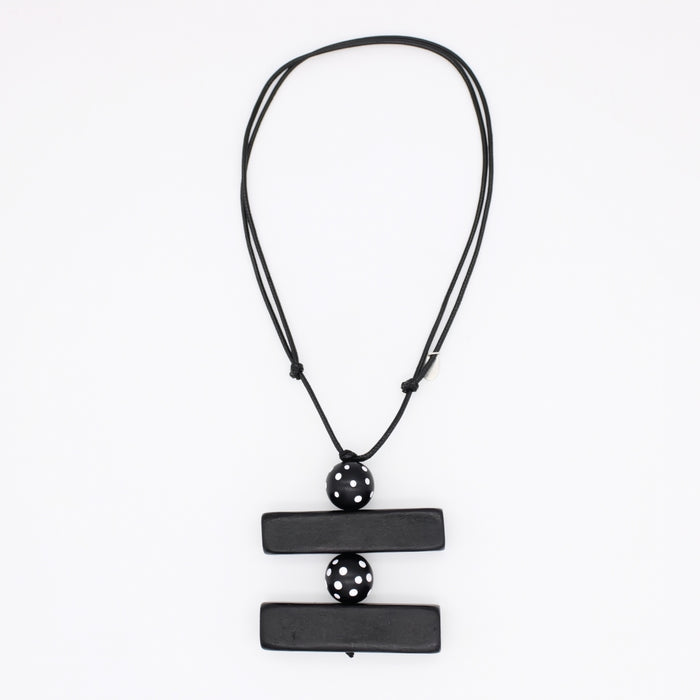 A black geometric pendant necklace featuring two horizontal rectangular bars connected by a central perforated sphere, suspended on a black cord against a plain white background.