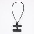 A black geometric pendant necklace featuring two horizontal rectangular bars connected by a central perforated sphere, suspended on a black cord against a plain white background.