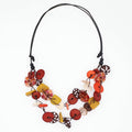 A multi-strand statement necklace featuring colorful faux buttons in red, orange, yellow, brown, and white, strung on a black cord against a plain white background.