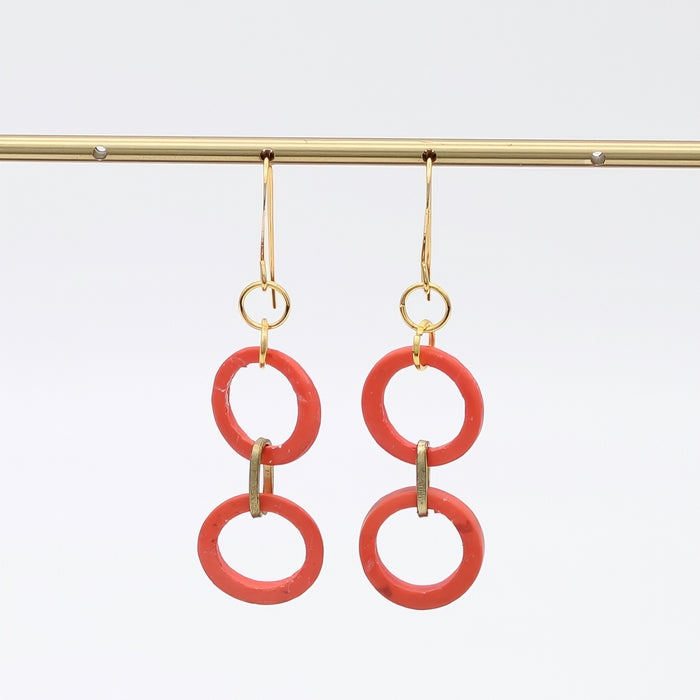 Pair of orange circular earrings with gold hooks on a white background
