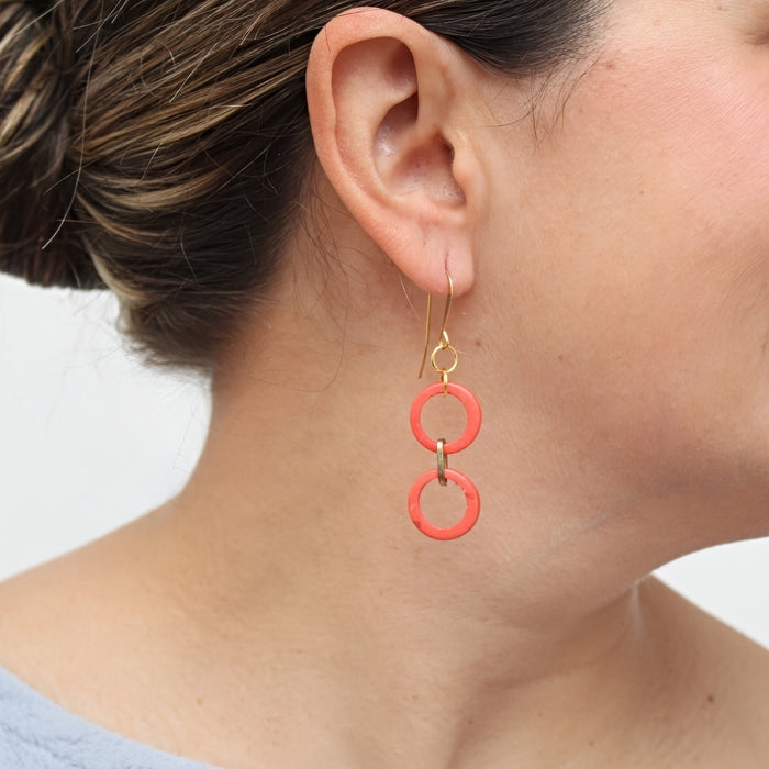 Close-up of a person wearing red hoop earrings with a neutral background