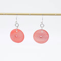 Pink circular earrings on a gold rod against a white background