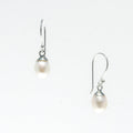 A pair of dainty silver hook earrings with white freshwater pearls attached, displayed against a white background.