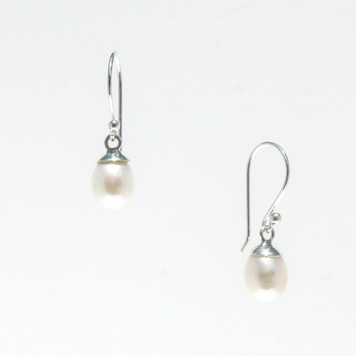 A pair of dainty silver hook earrings with white freshwater pearls attached, displayed against a white background.