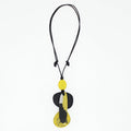 A modern abstract pendant necklace featuring a black cord and a multi-layered pendant with yellow, black, and white organic shapes, shown against a plain white background.