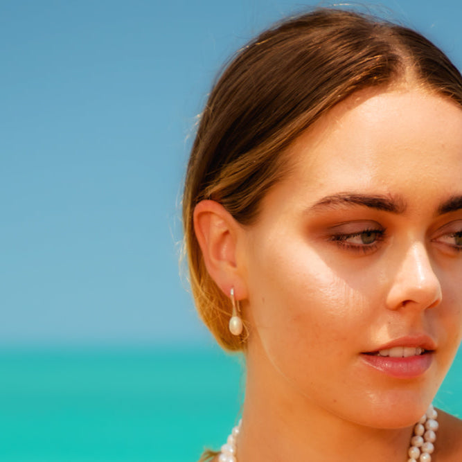 Woman wearing pearl earrings with a clear blue sky and turquoise water in the background