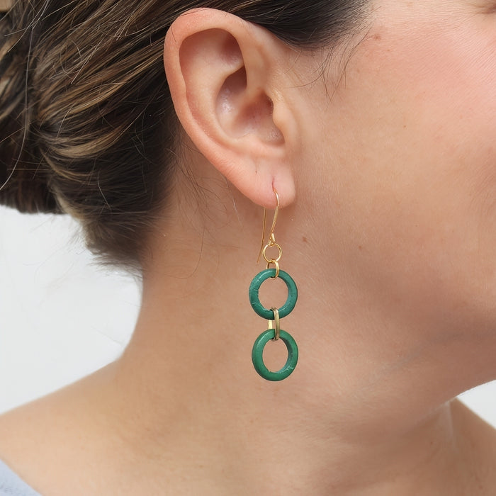 Green earrings worn by a person on a light background
