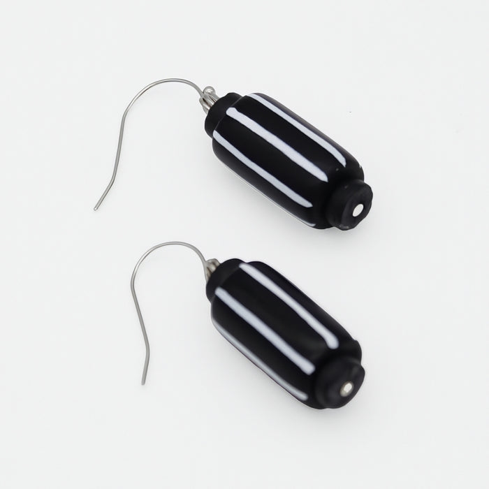A pair of drop earrings featuring glossy black cylindrical beads with three horizontal white stripes, suspended from silver fishhook wires on a plain white background.