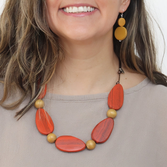 Woman wearing a orange and gold necklace with matching earrings on a plain background