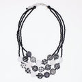 A multi-strand statement necklace featuring black beaded cords and a tiered arrangement of round beads in black, white, and gray patterns, including stripes, polka dots, and marbled textures, on a plain white background.