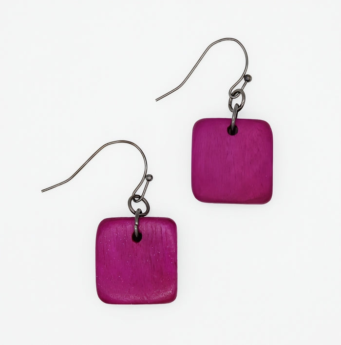 A pair of square-shaped drop earrings with a textured magenta-purple wooden disc and a dark metal fishhook ear wire, shown on a plain white background.
