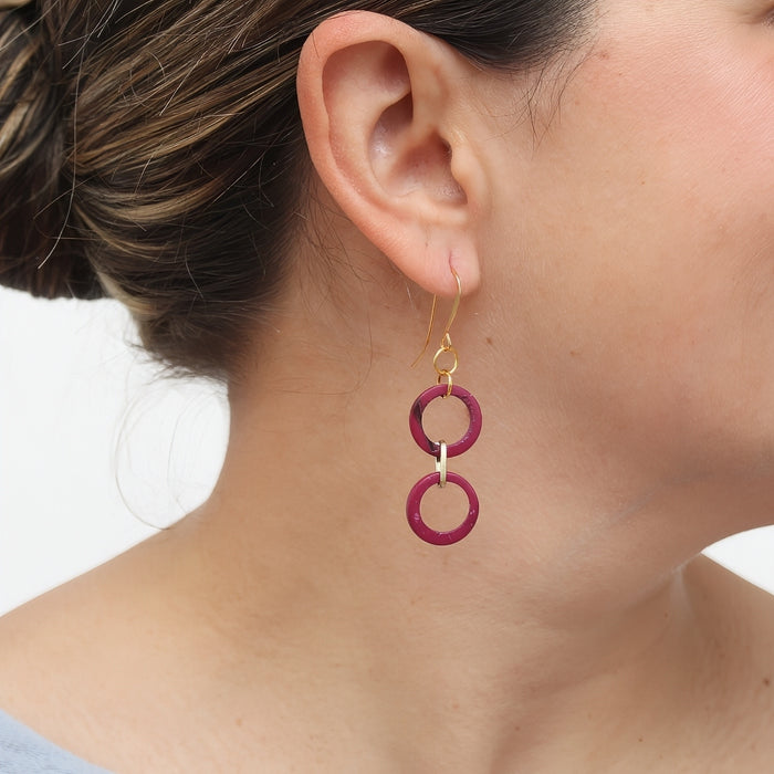 Close-up of a person wearing pink circular earrings with gold hooks.