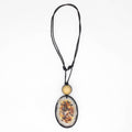 A black cord necklace featuring a large oval pendant with a dried floral or botanical inlay, accented by a small round gold bead above it, shown against a plain white background.