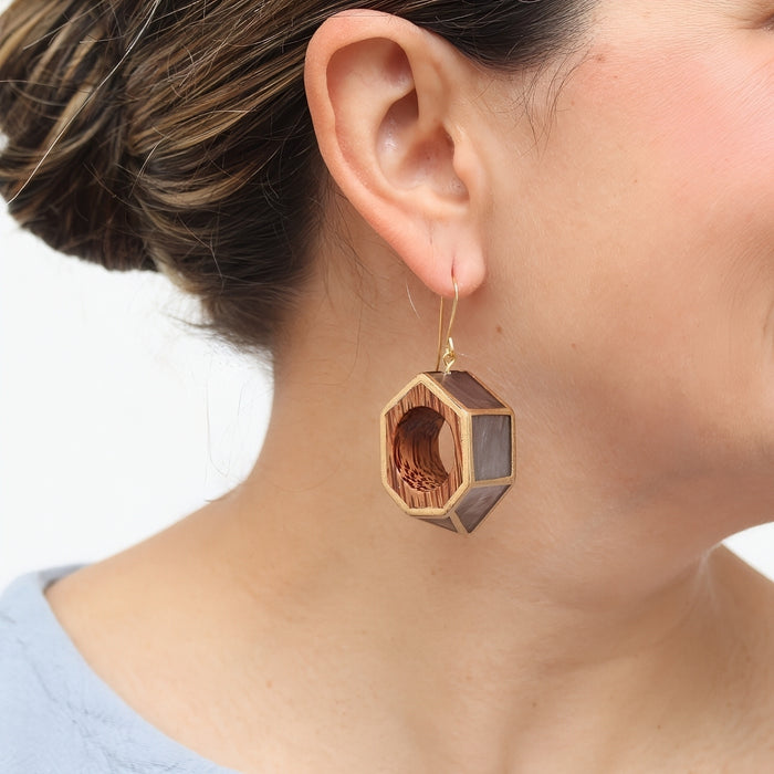 Wooden hexagonal earring worn by a person on a white background