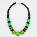 A beaded necklace featuring matte black round beads, vibrant green round beads, and striped lime green and black disc beads, with a silver clasp, shown on a plain white background.