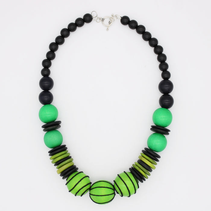 A beaded necklace featuring matte black round beads, vibrant green round beads, and striped lime green and black disc beads, with a silver clasp, shown on a plain white background.
