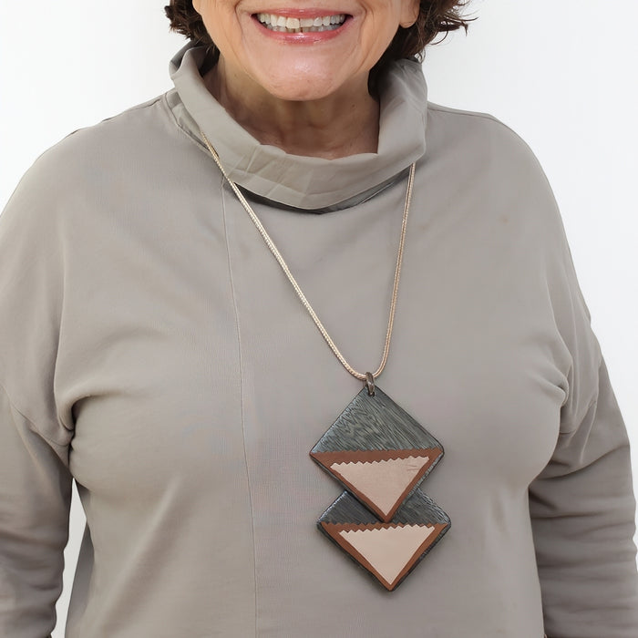 Woman wearing a necklace with geometric pendant on a plain background