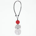 A modern multi-piece pendant necklace featuring a black cord, a solid red disc, a white disc with black polka dots, and a white disc with black diagonal lines, shown on a plain white background.
