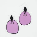A pair of handmade dangle earrings featuring irregular lavender purple glass chips with black edges, suspended from black beads on silver fishhook wires, set against a plain white background.