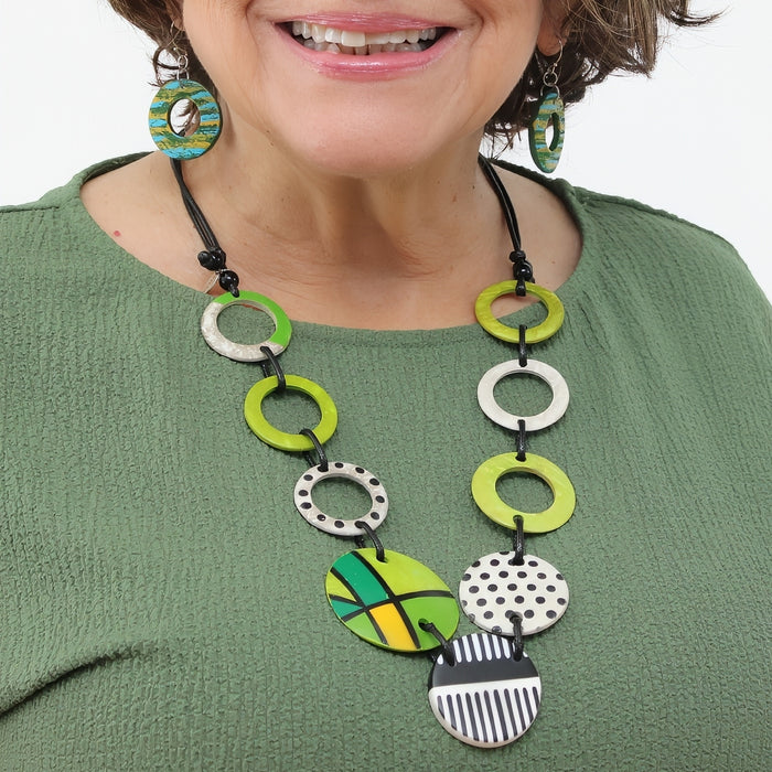 Woman wearing a colorful necklace with green, black, and white circular pendants on a white background