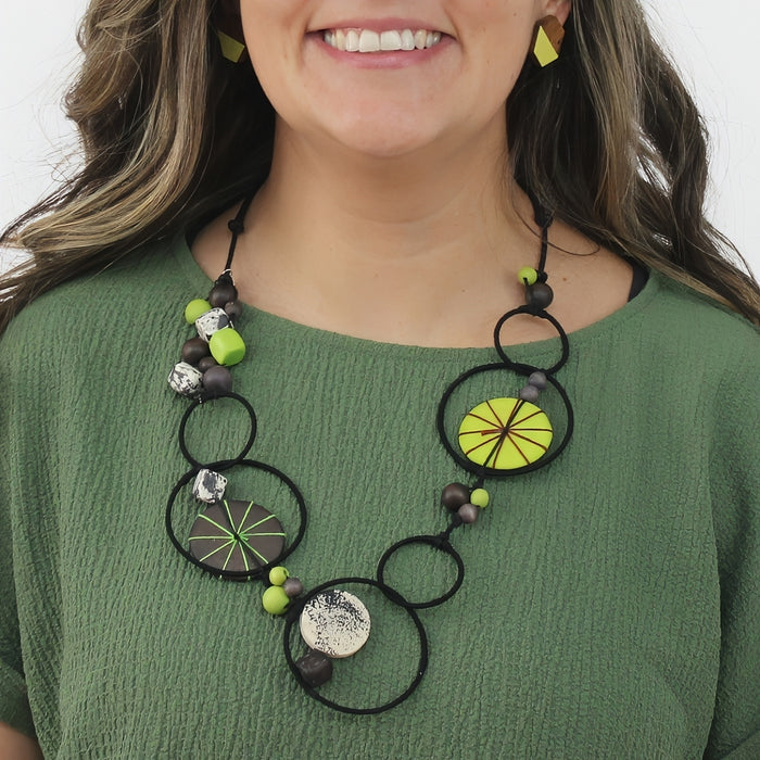 Woman wearing a green and black beaded necklace with circular designs.