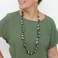 Woman wearing a green shirt with a long, colorful necklace against a white background