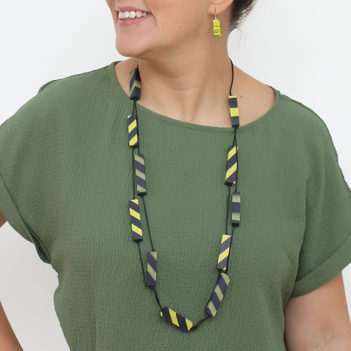 Woman wearing a green shirt with a long, colorful necklace against a white background