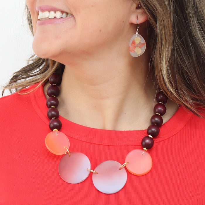 Woman wearing a colorful necklace with pink and purple circular beads on a red shirt.