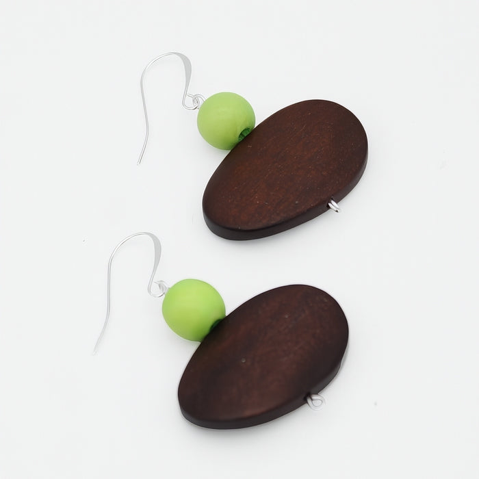 A pair of dangle earrings featuring dark brown wooden oval pendants and a small light green bead suspended below, hanging from silver fishhook wires on a plain white background.