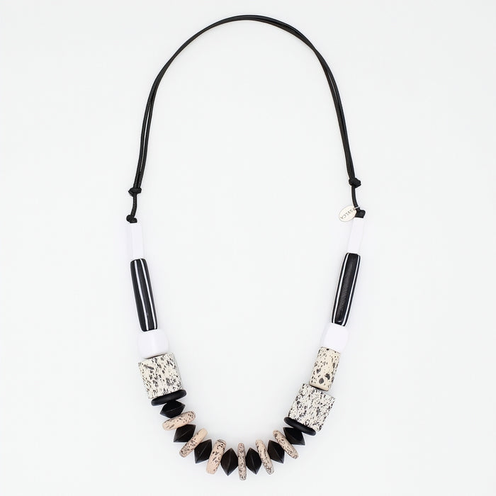 A statement necklace featuring a black cord, white cylindrical beads, black striped beads, and textured black and beige geometric beads, displayed on a clean white background.