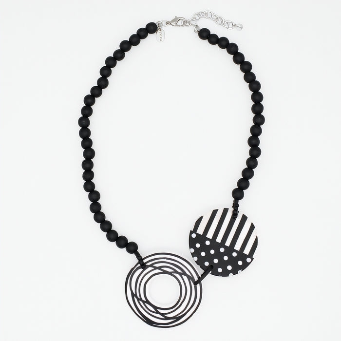 A black beaded statement necklace featuring two circular pendant elements: one with black and white stripes and one with black and white polka dots, displayed on a clean white background.