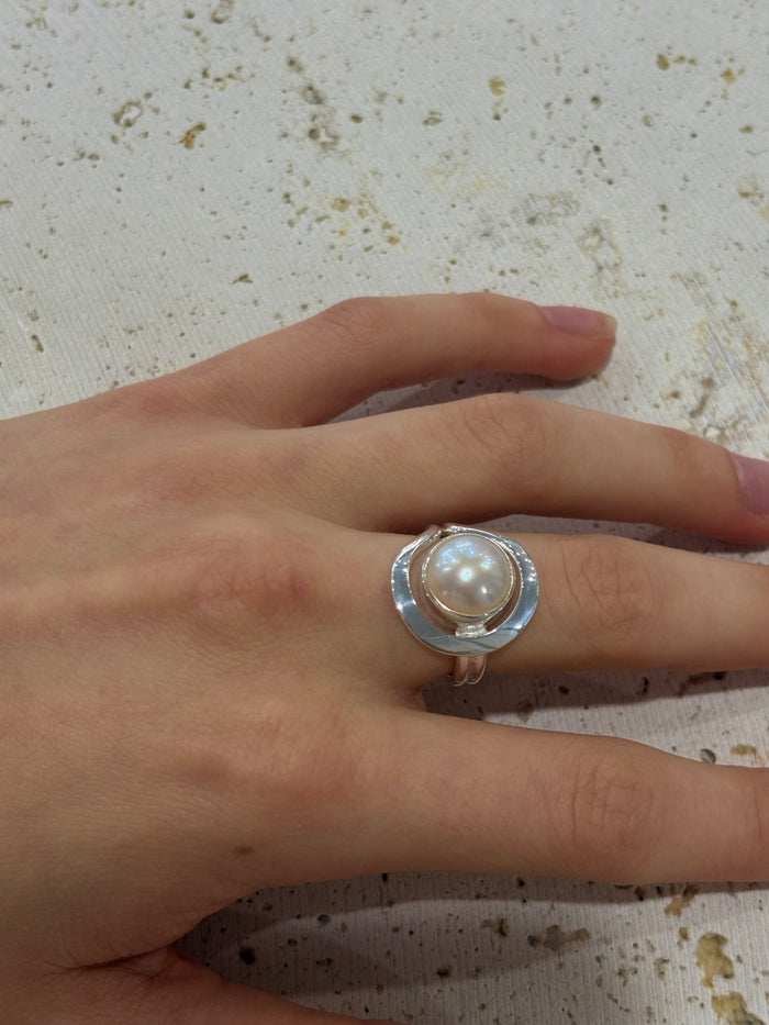 Hand wearing a ring with a pearl on a textured surface