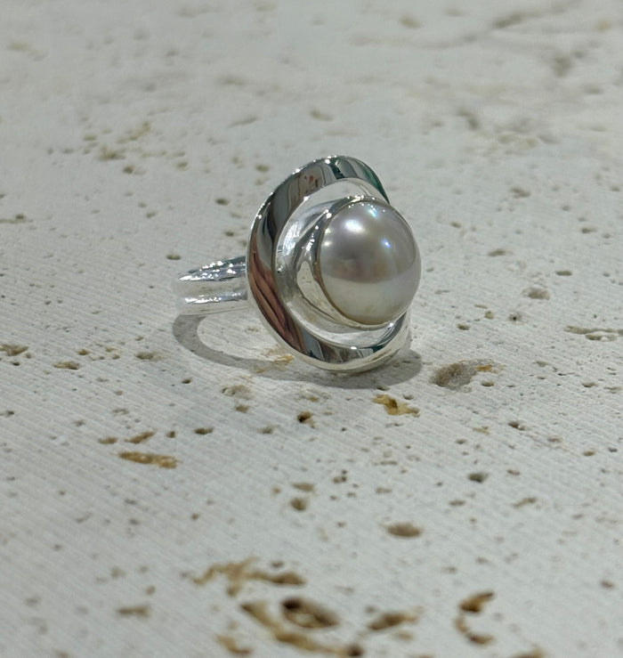 Silver ring with a pearl on a textured beige surface