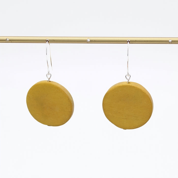 Mustard yellow circular earrings hanging on a gold rod against a white background