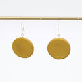 Mustard yellow circular earrings hanging on a gold rod against a white background