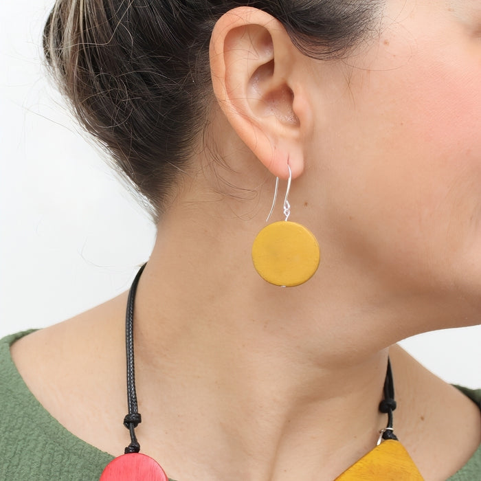 Close-up of a person wearing colorful earrings with a plain background