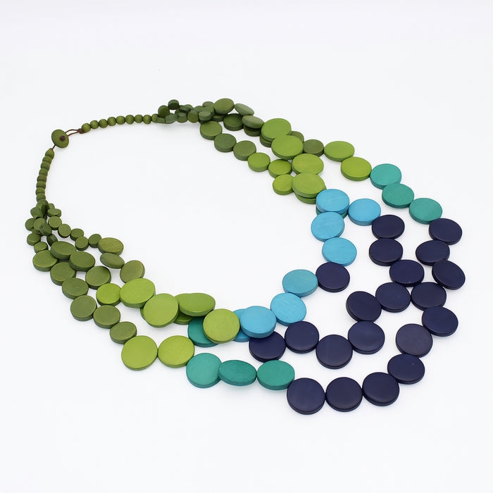 A multi-strand disc necklace made of flat circular beads in shades of olive green, lime green, turquoise, teal, and dark navy blue, arranged on a plain white background.