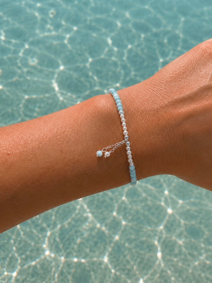 Light blue gemstone and freshwater pearl bracelet featuring delicate white pearls, soft blue beads and sterling silver accents on an adjustable design. A beach-inspired bracelet handcrafted for effortless coastal style.
