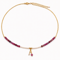 A delicate gold chain necklace featuring a row of ruby beads, pearl beads, and a small dangling charm